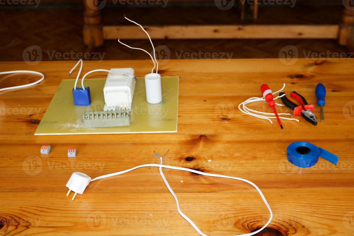 circuito eléctrico con cables y piezas de repuesto, equipo de instalación, alicates, cinta eléctrica azul, destornilladores sobre la mesa foto