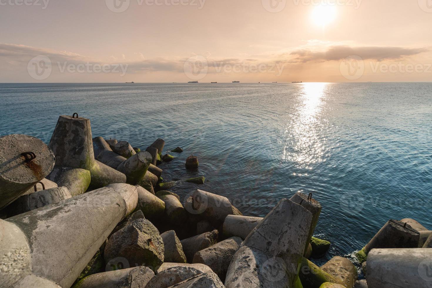 Beautiful sunset seascape. Travel dreams and motivation. Breakwaters tetrapods on shore of pier. Cargo ships on the horizon. photo