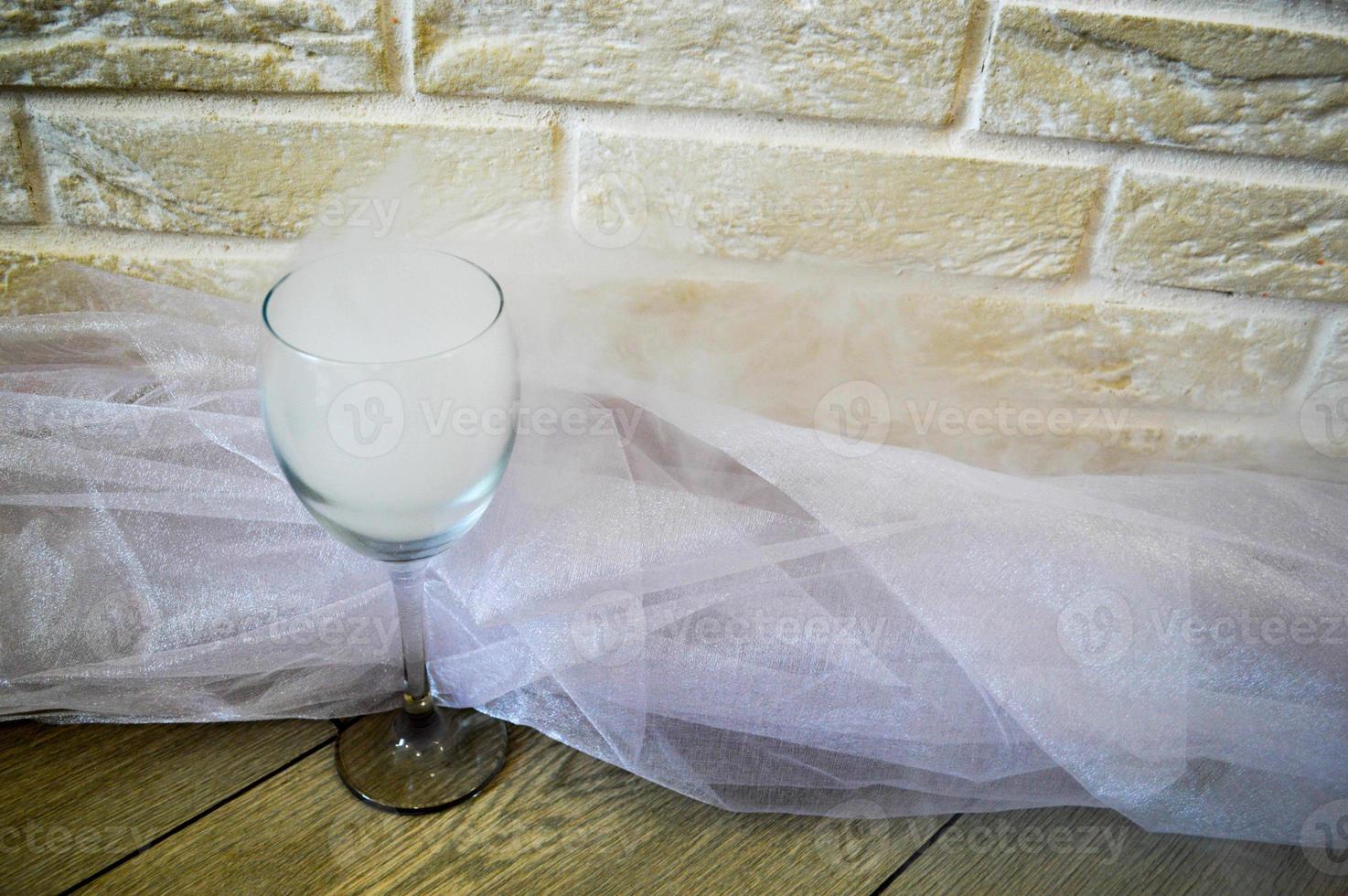 Steam in a transparent glass of wine on a background of beige brick wall and white fabric. Smoke in the glass. photo