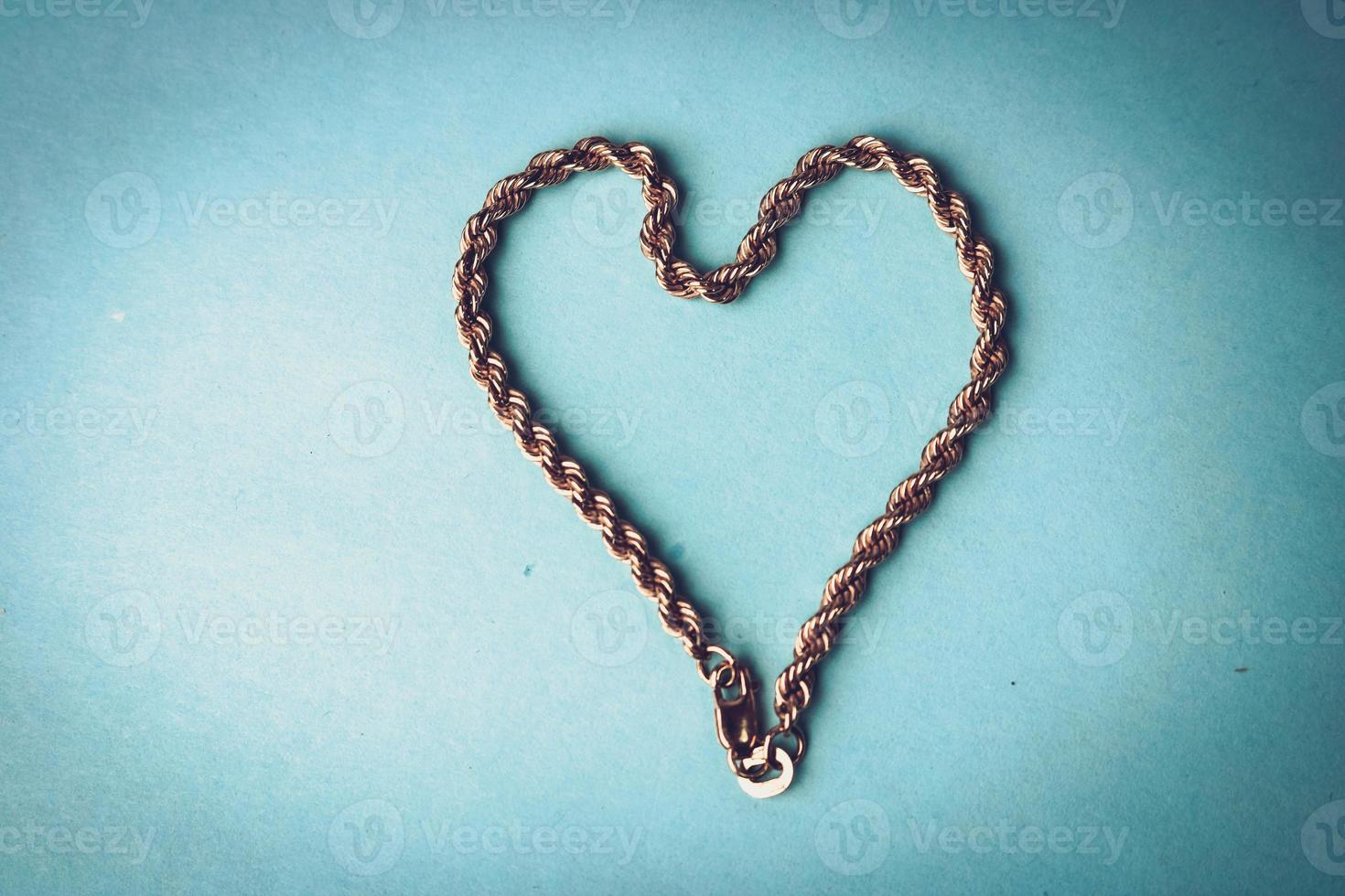 Texture of a beautiful golden dear festive chain of unique weaving in the shape of a heart on a blue background and copy space. Concept love, marriage proposal, marriage, St. Valentine's Day photo