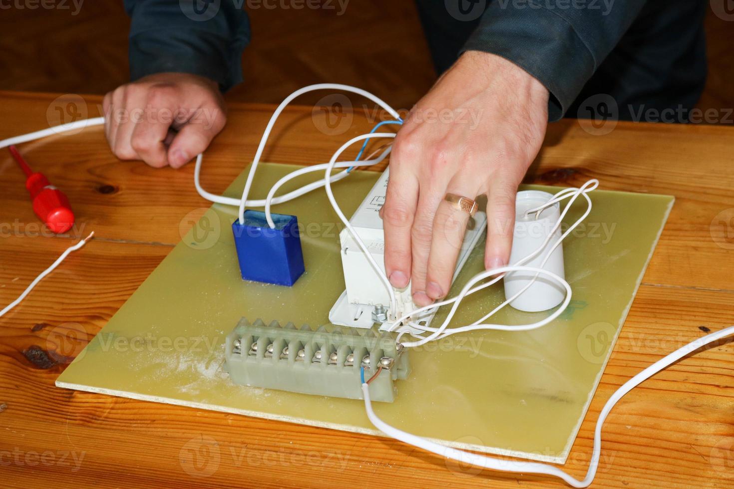 A man working electrician works, collects the electric circuit of a large white street lamp with wires, a relay at an industrial plant factory photo