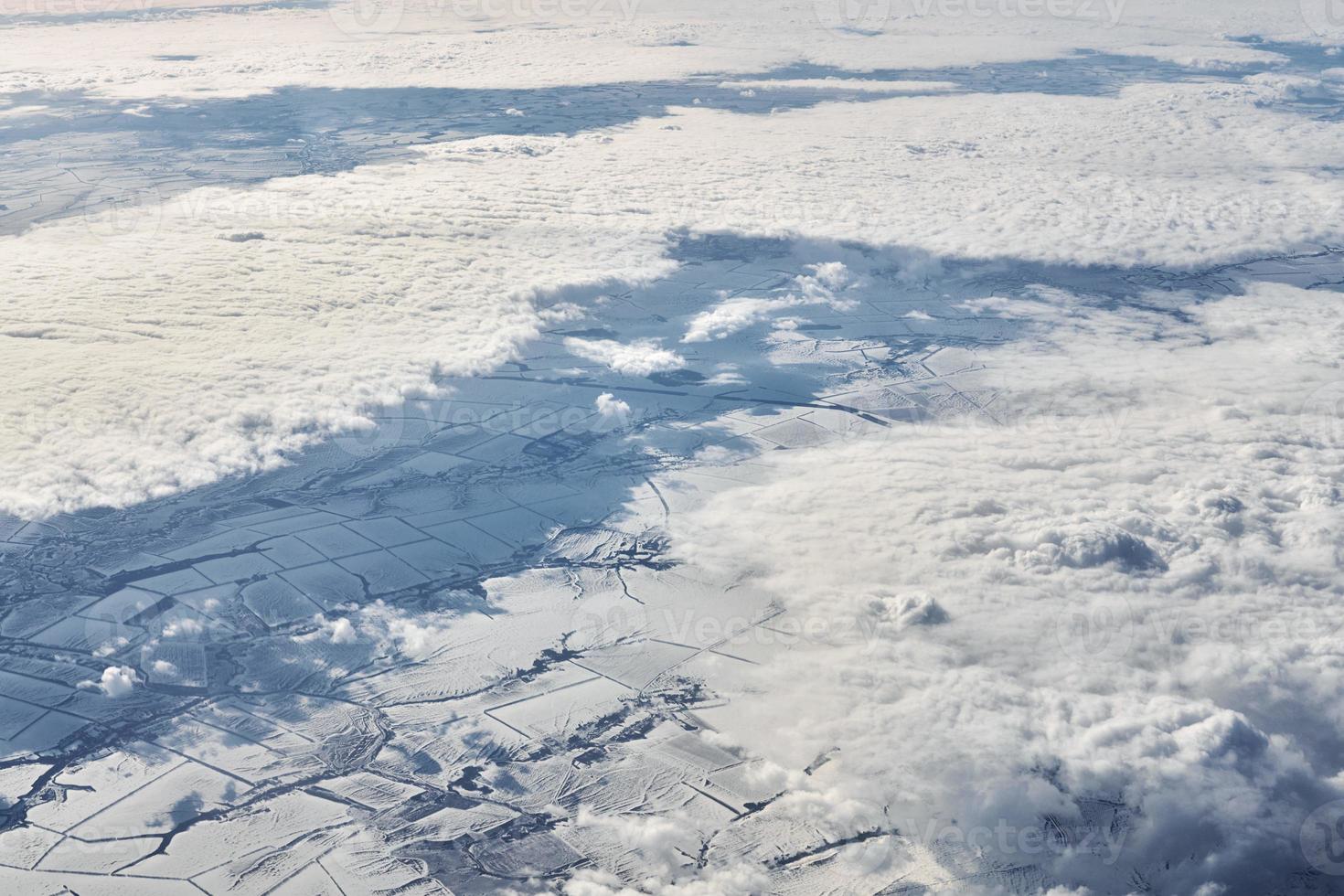Aerial view over clouds top to snow covered rivers, fields and roads, winter fresh frosty air photo