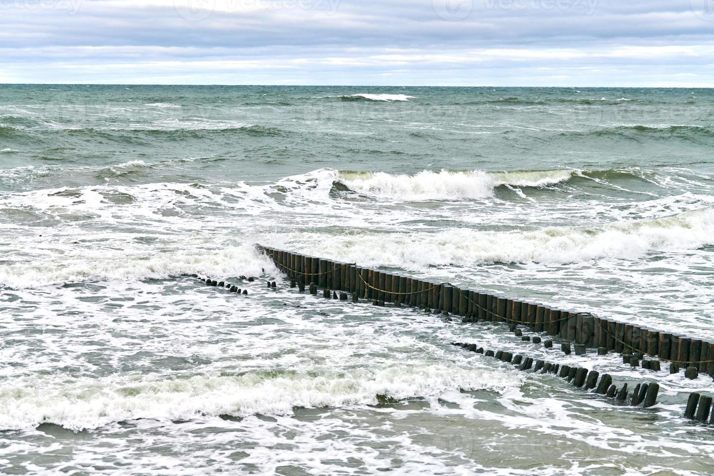 View of blue sea with foaming waves and wooden breakwaters photo