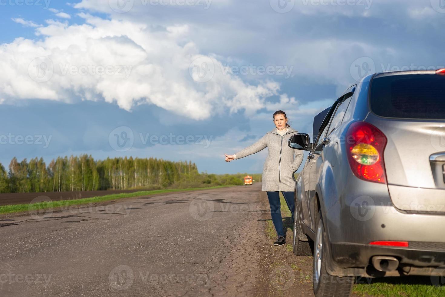 A woman in a jacket is trying to fix a broken car on the road. photo