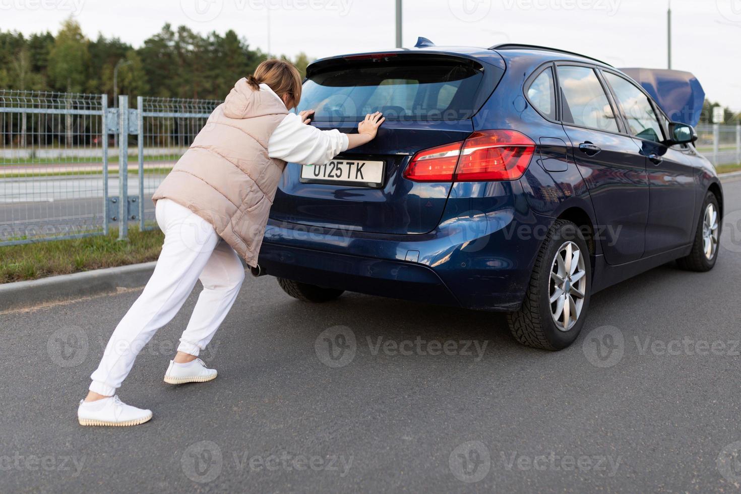 a woman pushes a broken down car from behind leaning on the trunk lid, traffic accident concept photo