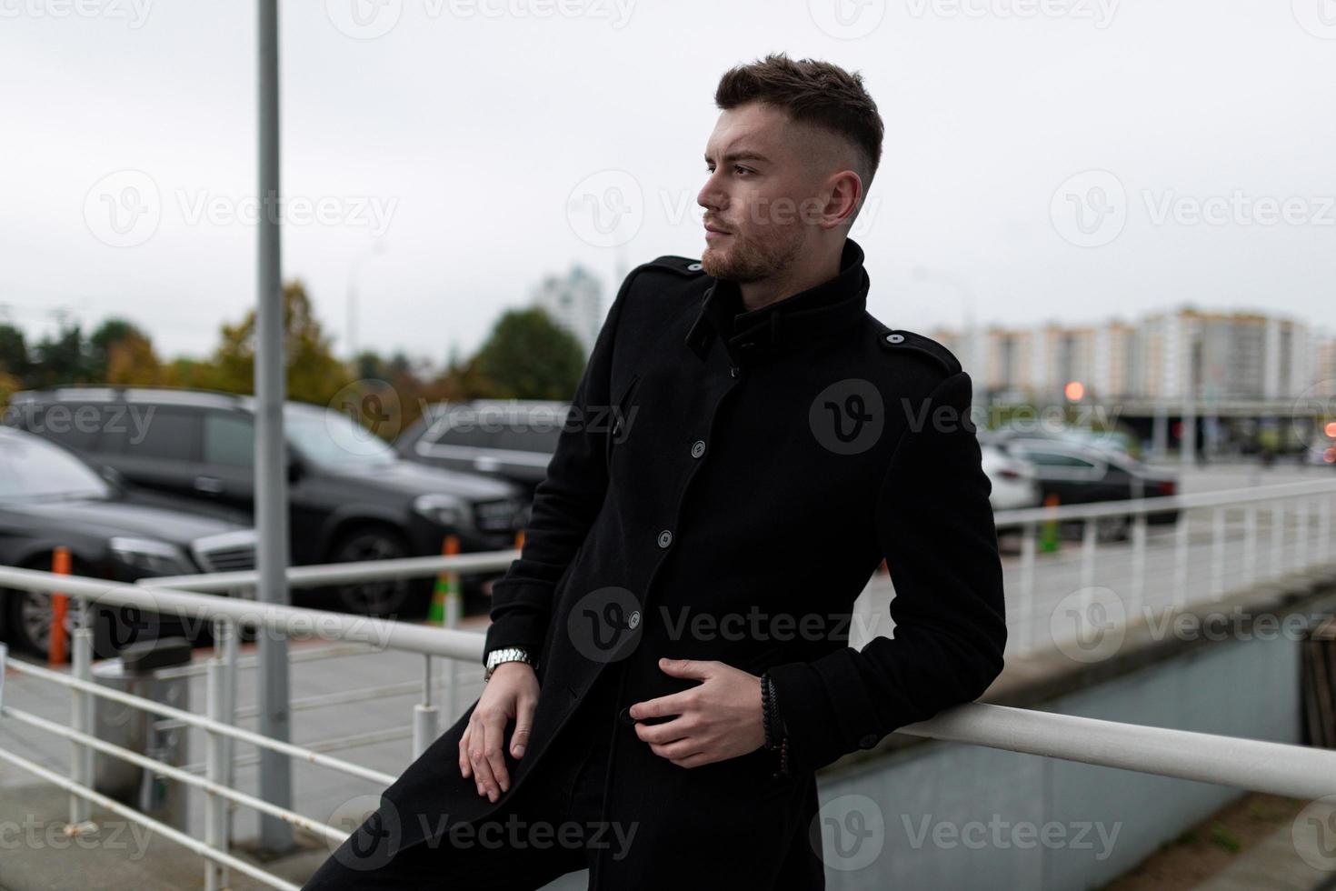 hombre de negocios con estilo en un abrigo negro en el fondo de un estacionamiento foto