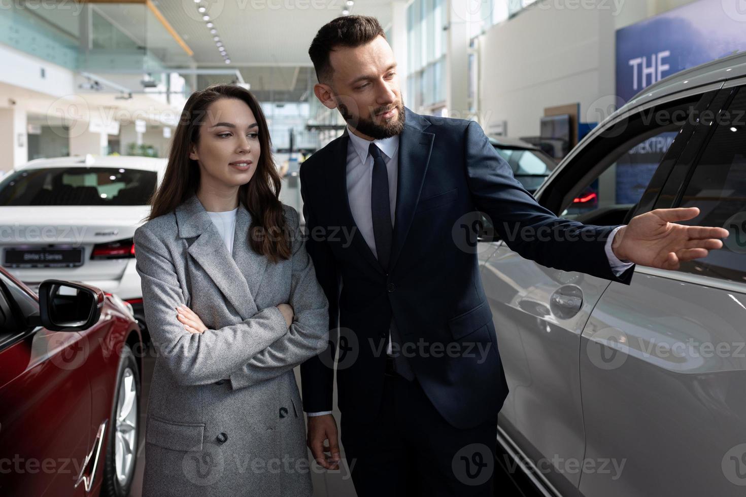 car dealership representative presenting a new car to a young woman buyer photo