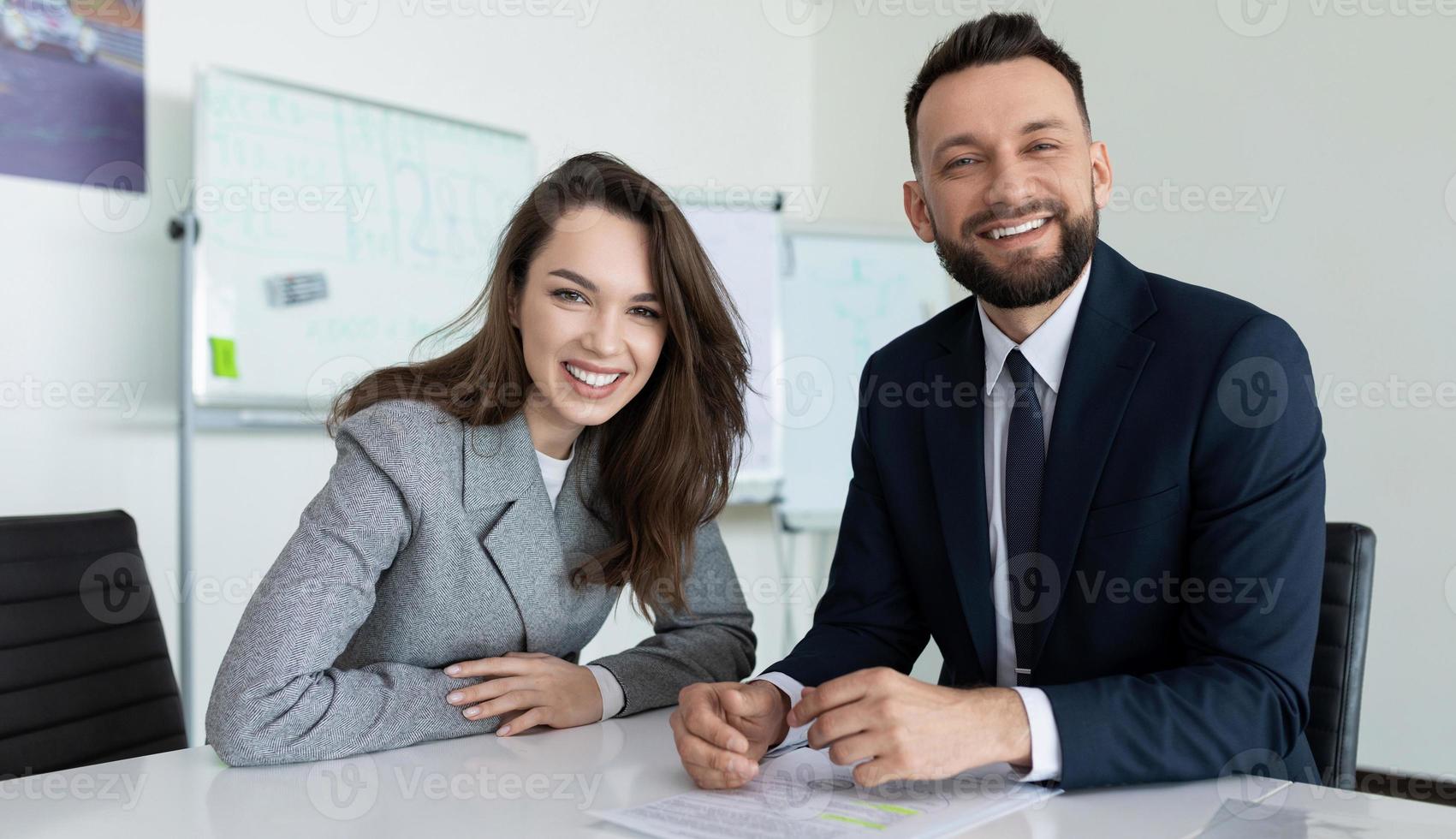 man and woman employees of the company in presentable business clothes with a smile look at the camera while sitting at the table photo