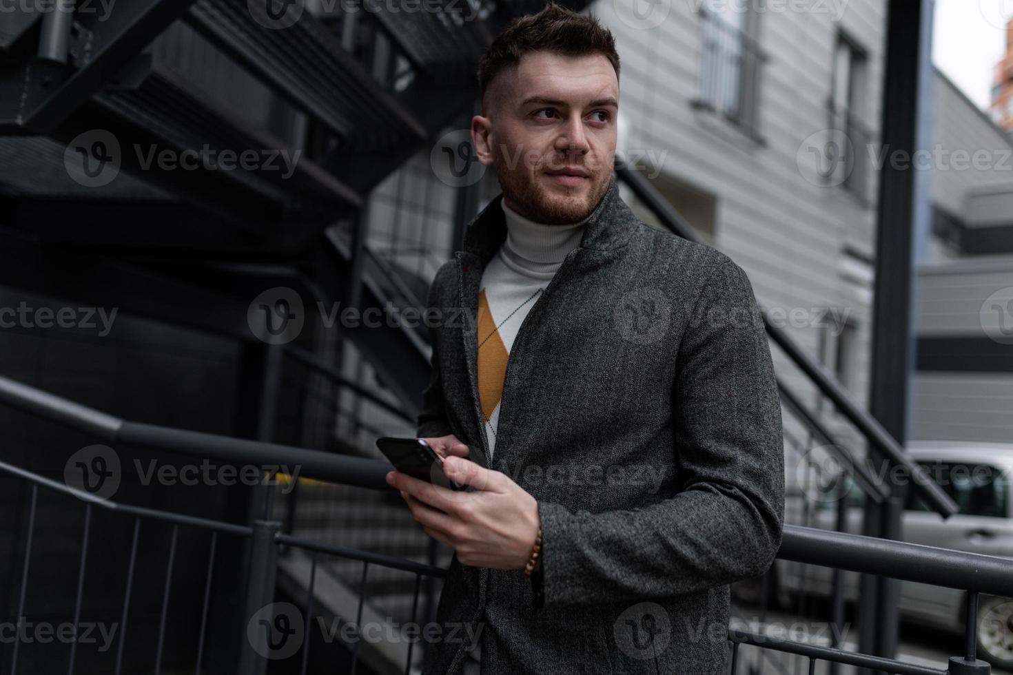 successful businessman entrepreneur in a stylish gray coat and a mobile phone in his hands photo