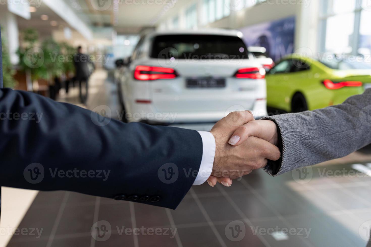 buyer and seller at car dealership shaking hands after buying a car photo