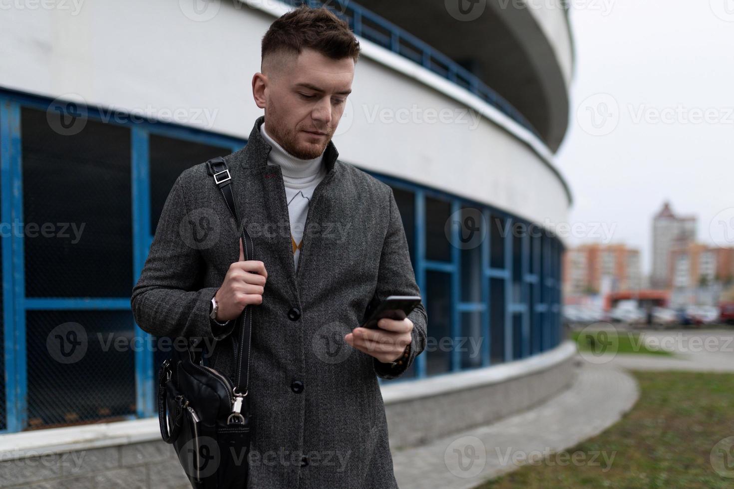 young man with a mobile phone and a business bag on the background of a parking lot photo
