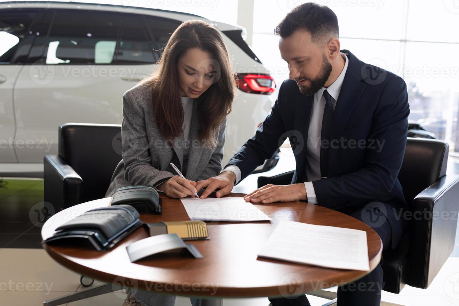 mujer joven y gerente de ventas de automóviles firman un contrato foto