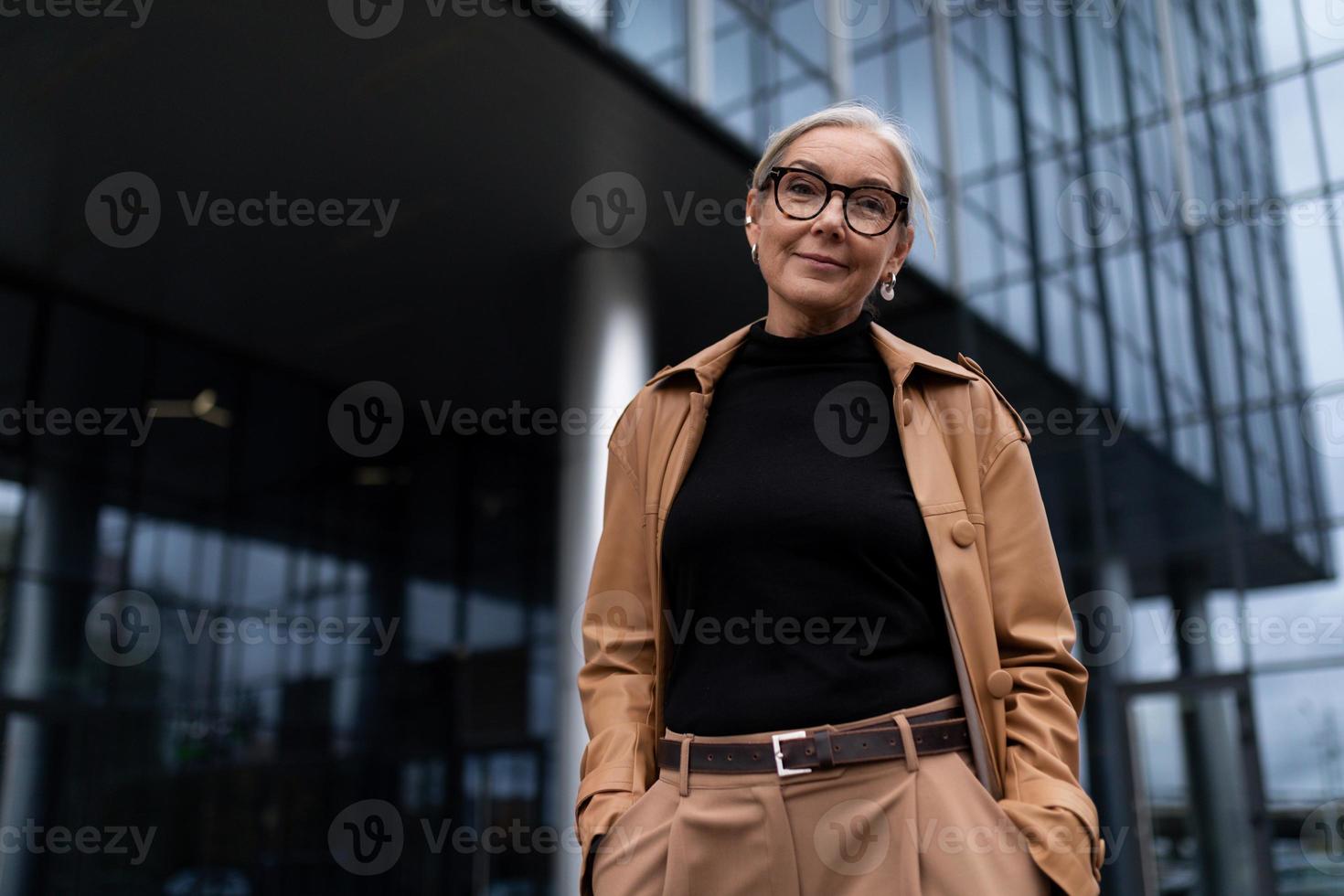mujer de negocios de alto nivel en el fondo de un edificio de oficinas mira a la cámara con una sonrisa foto