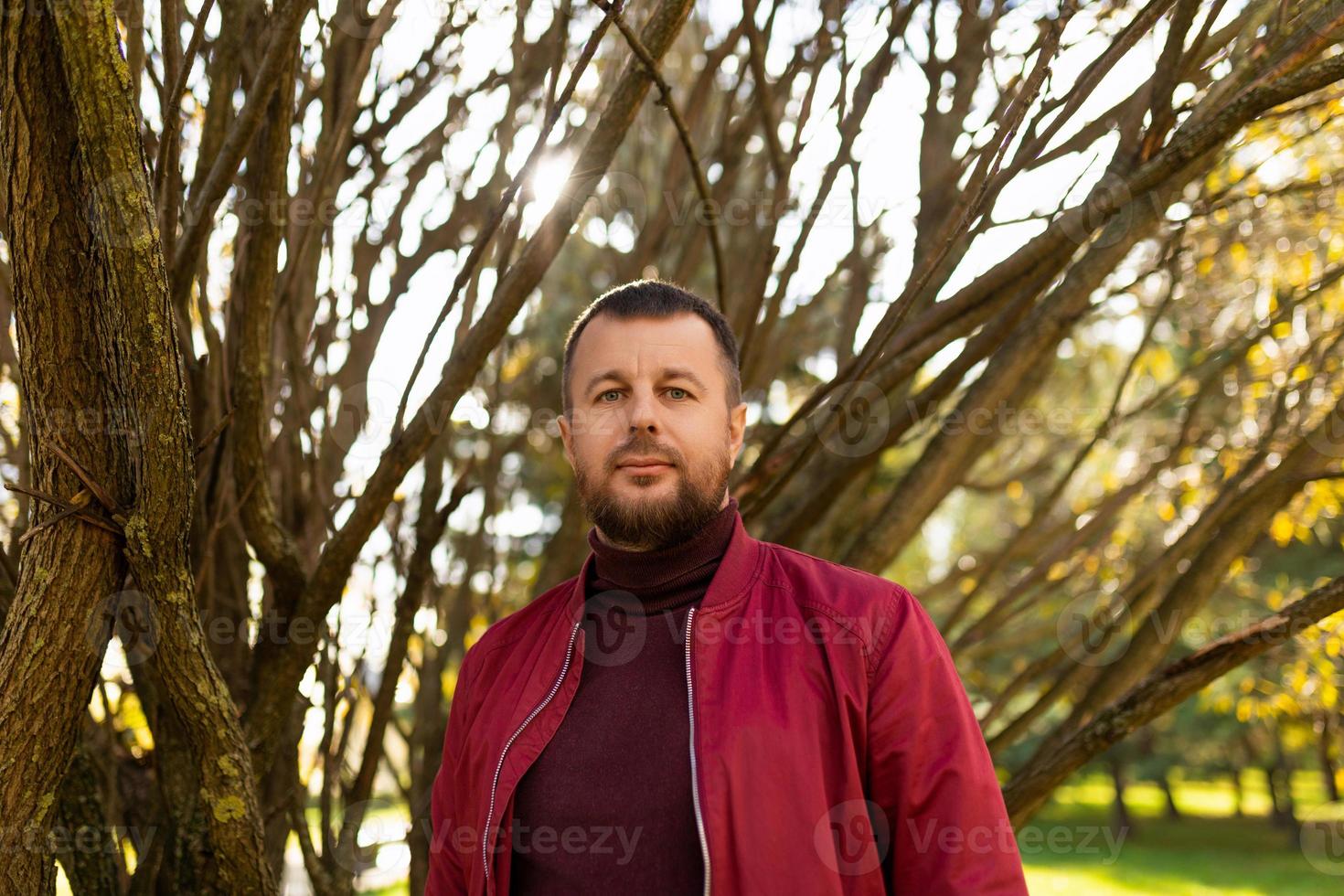 retrato de un hombre barbudo fuerte con una chaqueta roja en el parque de otoño foto