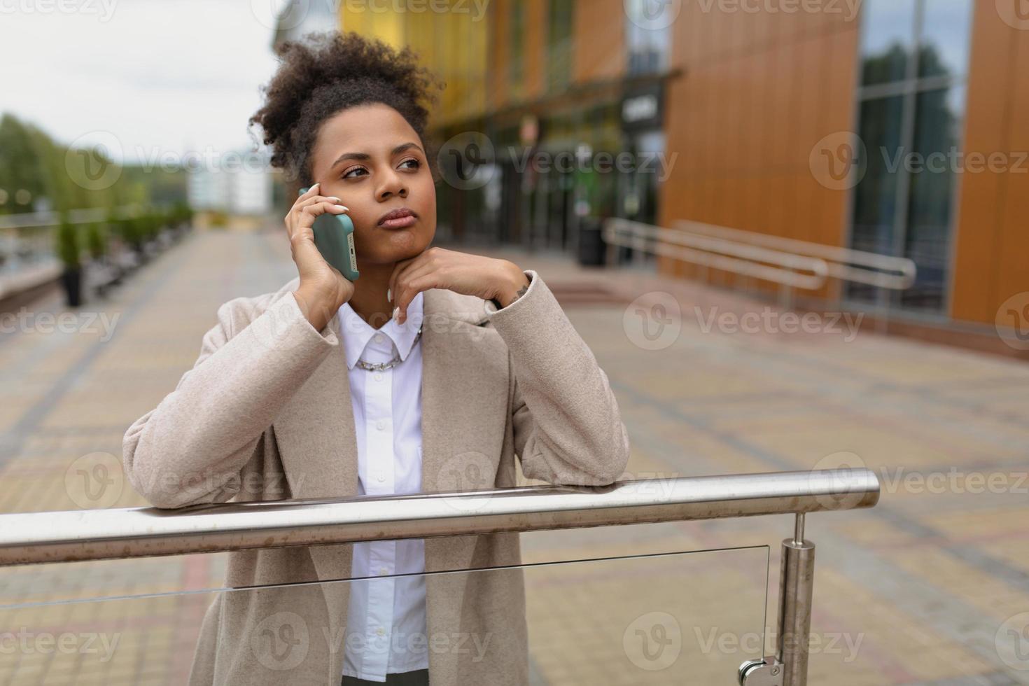 joven afroamericana seria hablando por un teléfono móvil en el contexto de un edificio administrativo foto
