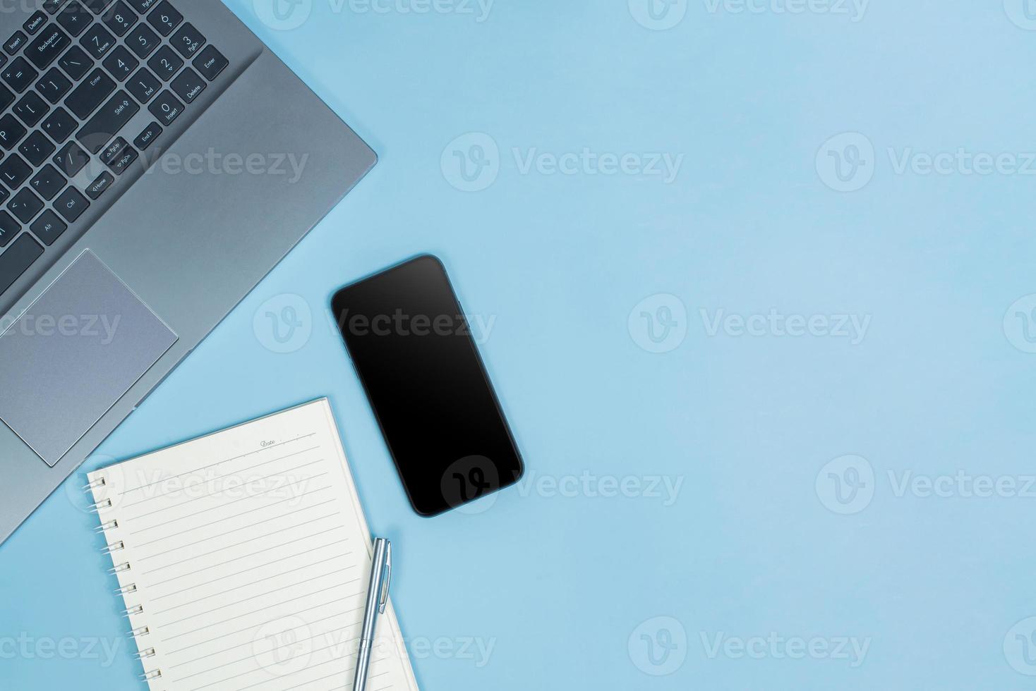 Top view of Office Table top with laptop computer, pen, balck smart phone and notebook with space photo