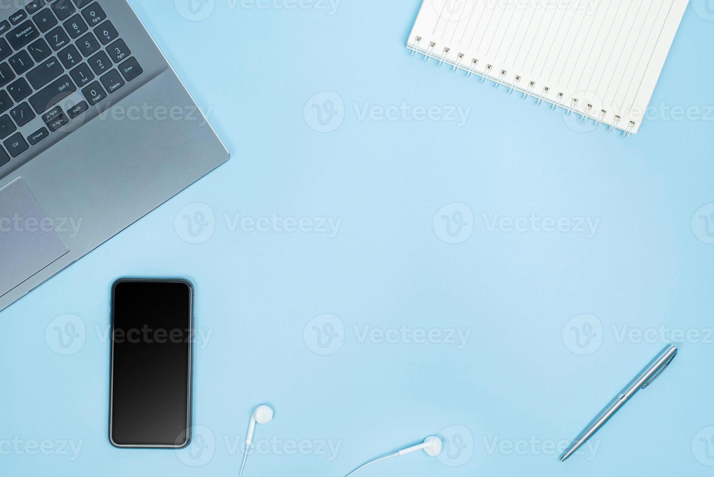 Top view of Office Table top with laptop computer, notebook, smart phone, pen, head phones on blue table with space photo