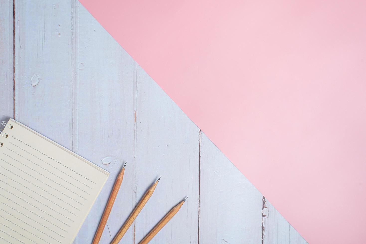 Top view image of notebook with pencils on wooden table with pink background photo