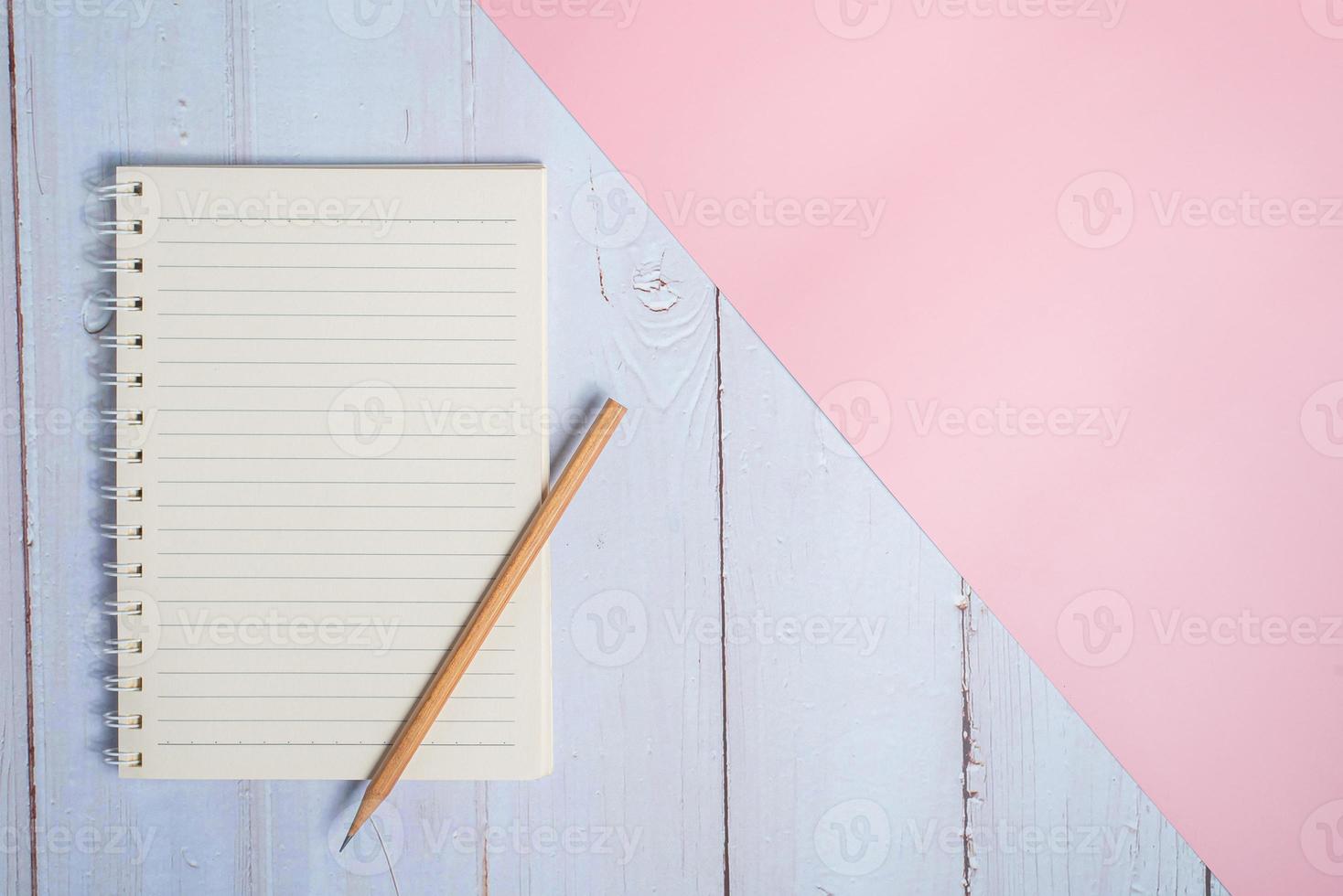 Top view image of notebook with pencil on wooden table with pink background photo