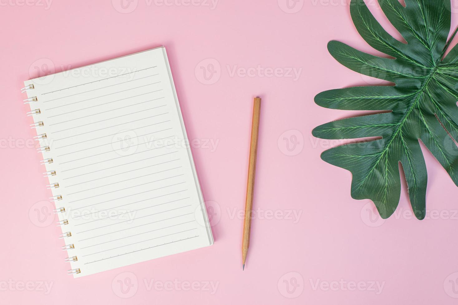 Top view image of notebook with pencils and xanadu leaf on pink background photo