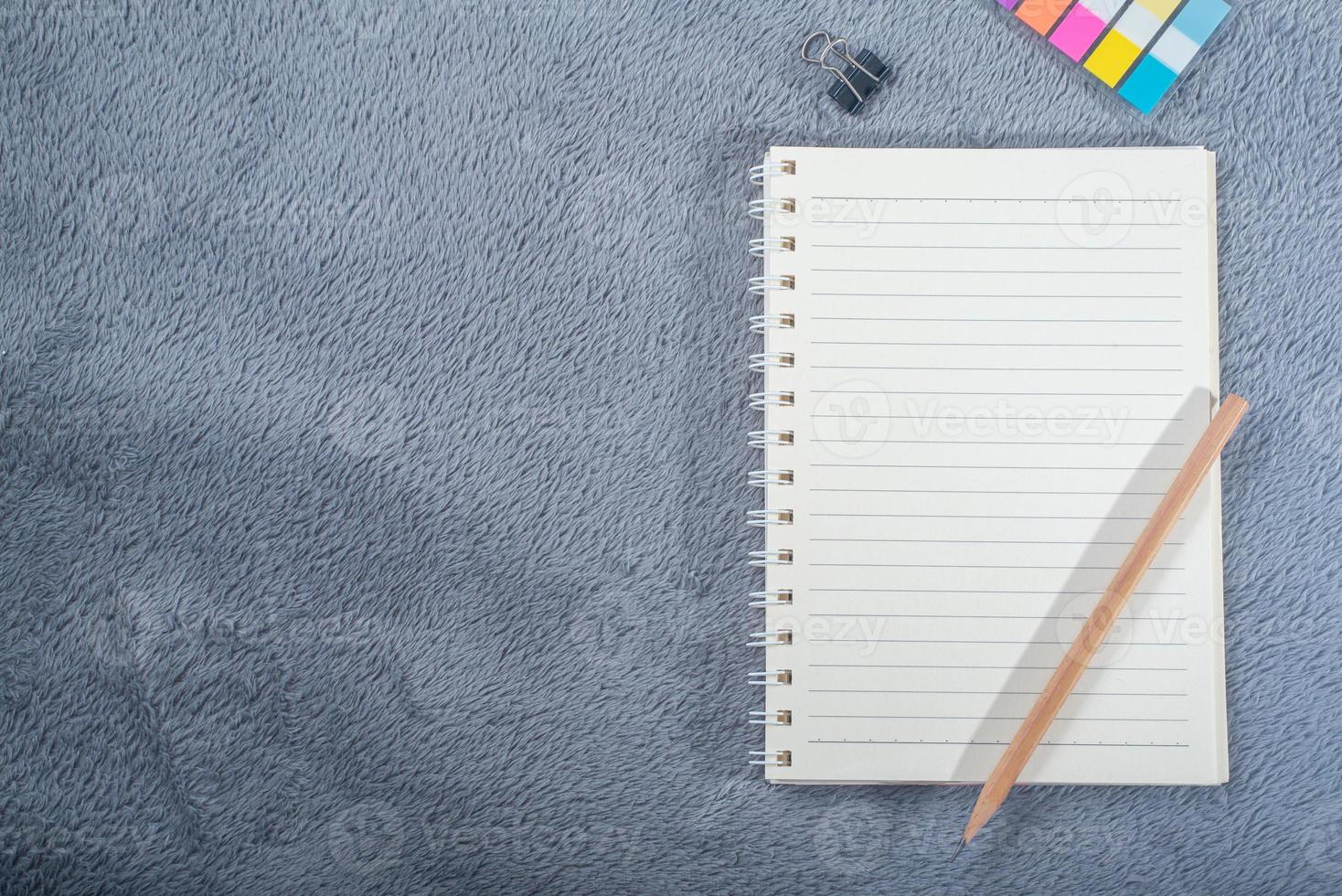 Top view image of notebook with pencil, colorful mini paper note and paper clip on gray carpet photo