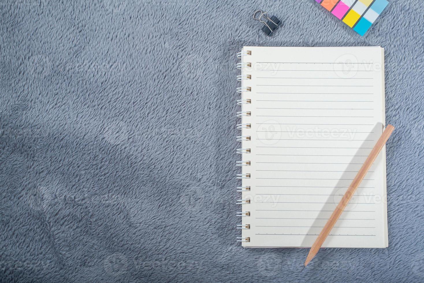 imagen de la vista superior del cuaderno con lápiz, mini nota de papel de colores y clip de papel en la alfombra gris foto