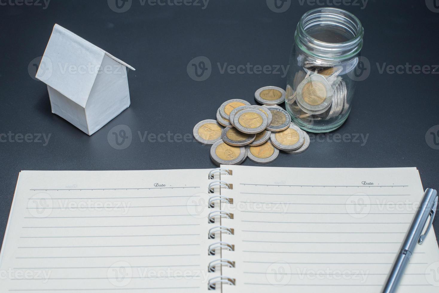 Thailand coins in jar with heap coins on black background with house model photo