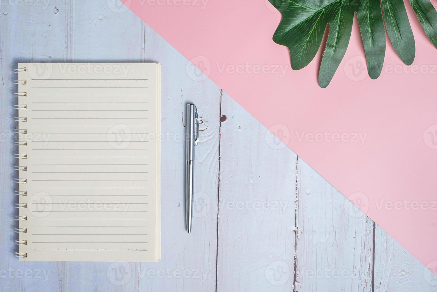 Top view image of notebook with pen and xanadu leaf on wooden table with pink background photo