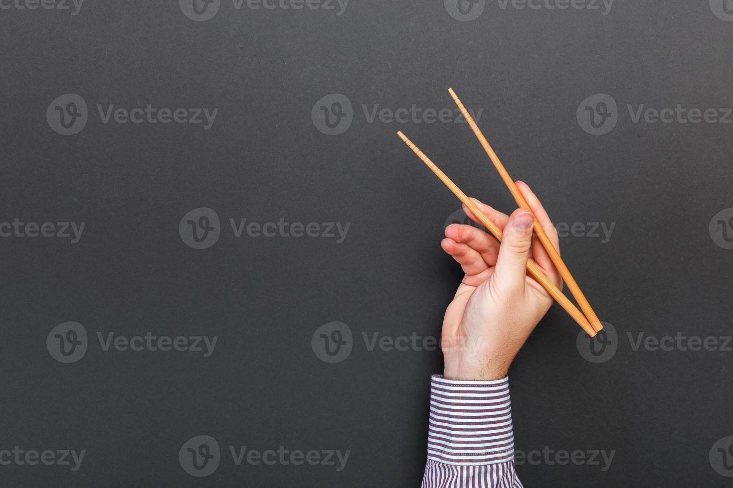 Creative image of wooden chopsticks in male hands on black background. Japanese and chinese food with copy space photo