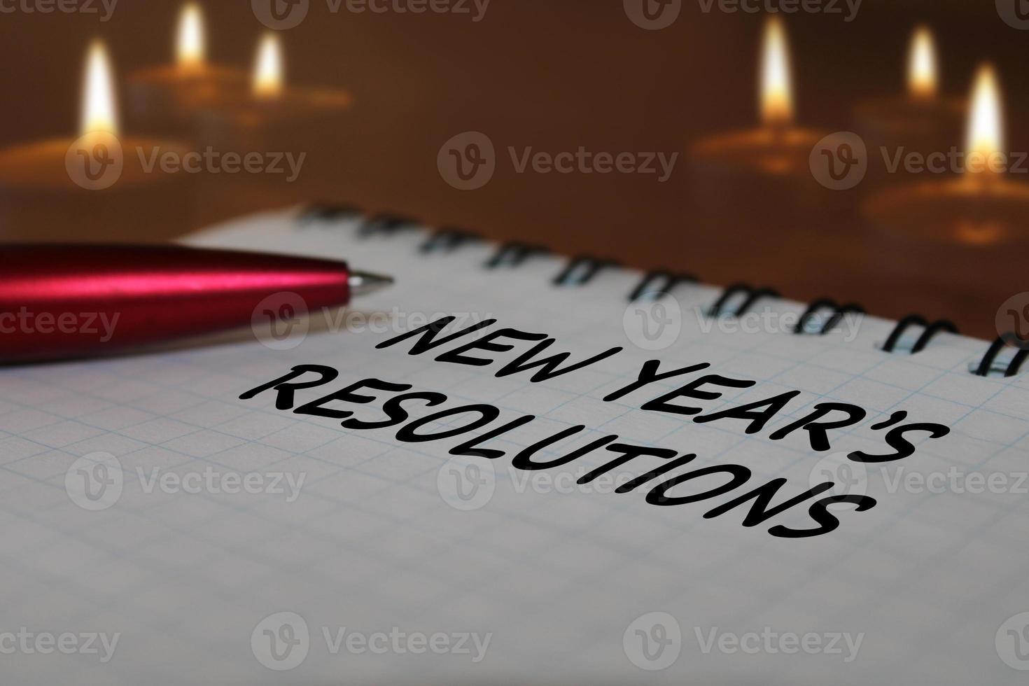 Notebook with a pen on a wooden table against the background of burning candles. The concept of resolutions for the new year. photo