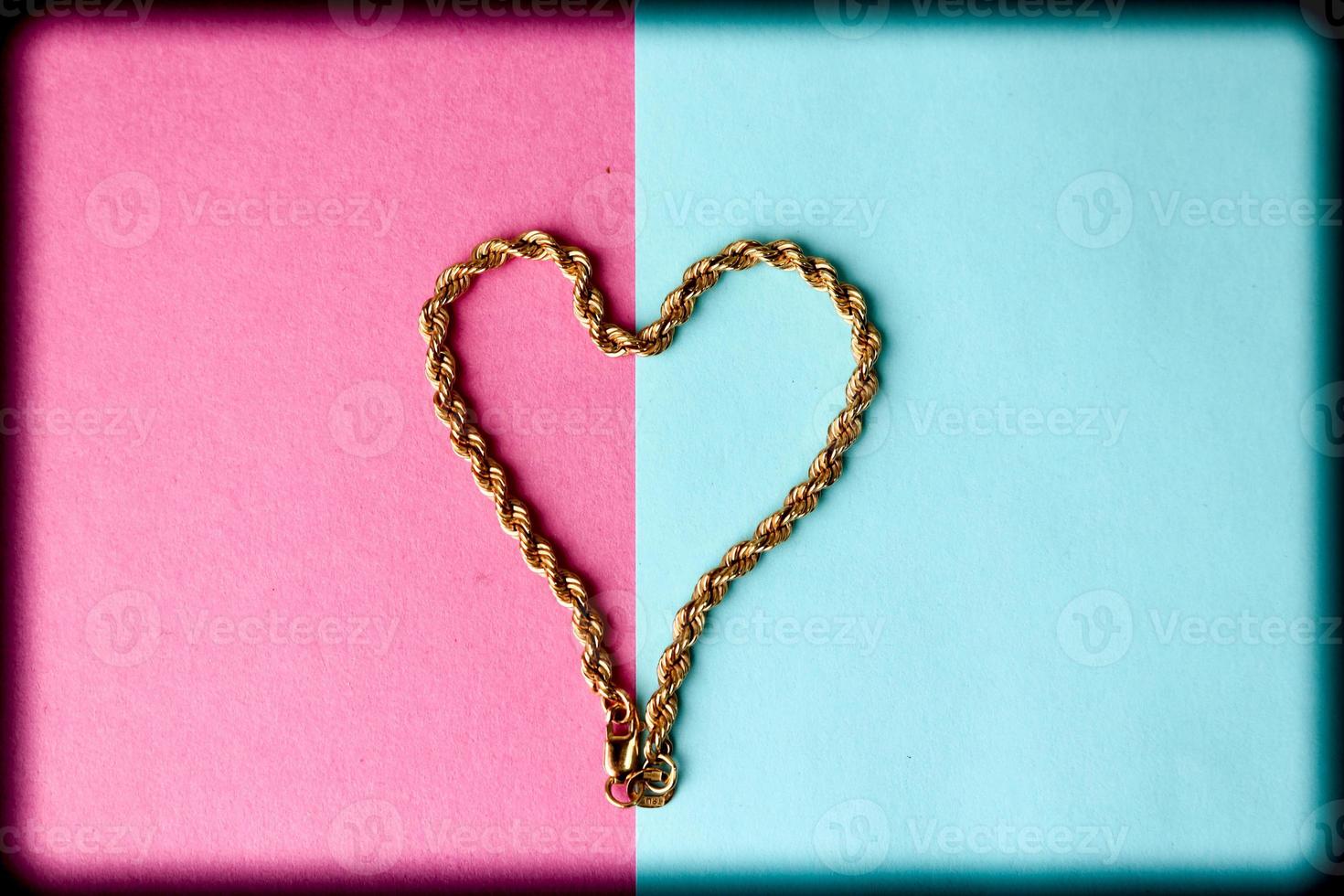 Texture of a beautiful golden festive chain unique weaving in the shape of a heart on a pink purple blue background and copy space. Concept love, marriage proposal, marriage, St. Valentine's Day photo