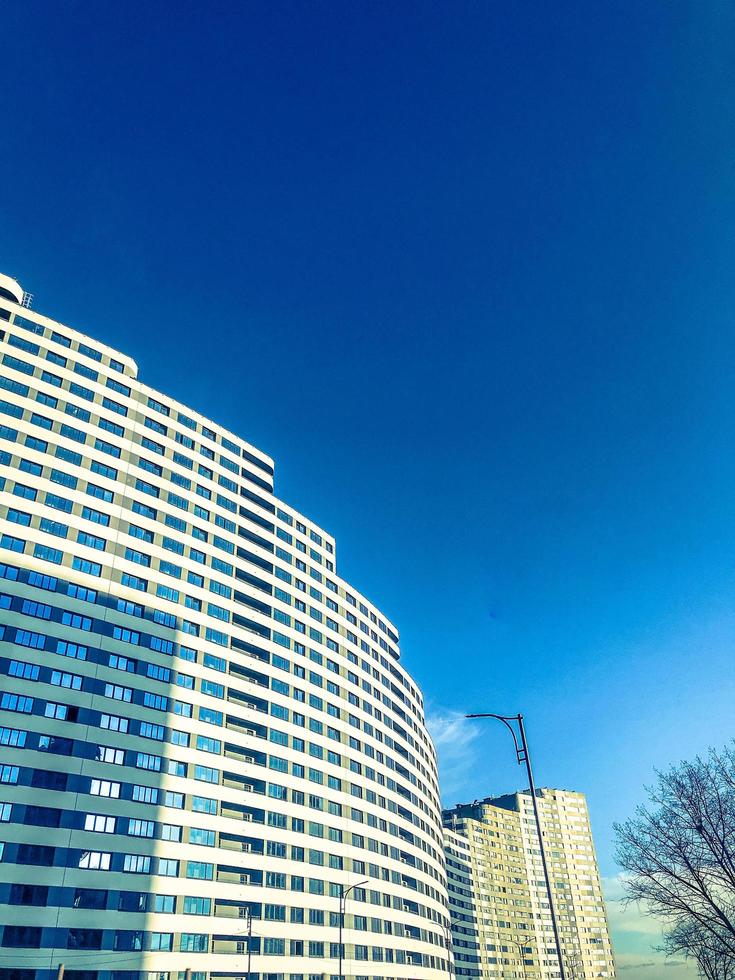 white long house in the form of a wave against a blue bright sky. new building of blocks of light colors, with glass windows on one level. unusual fashionable design of the new photo