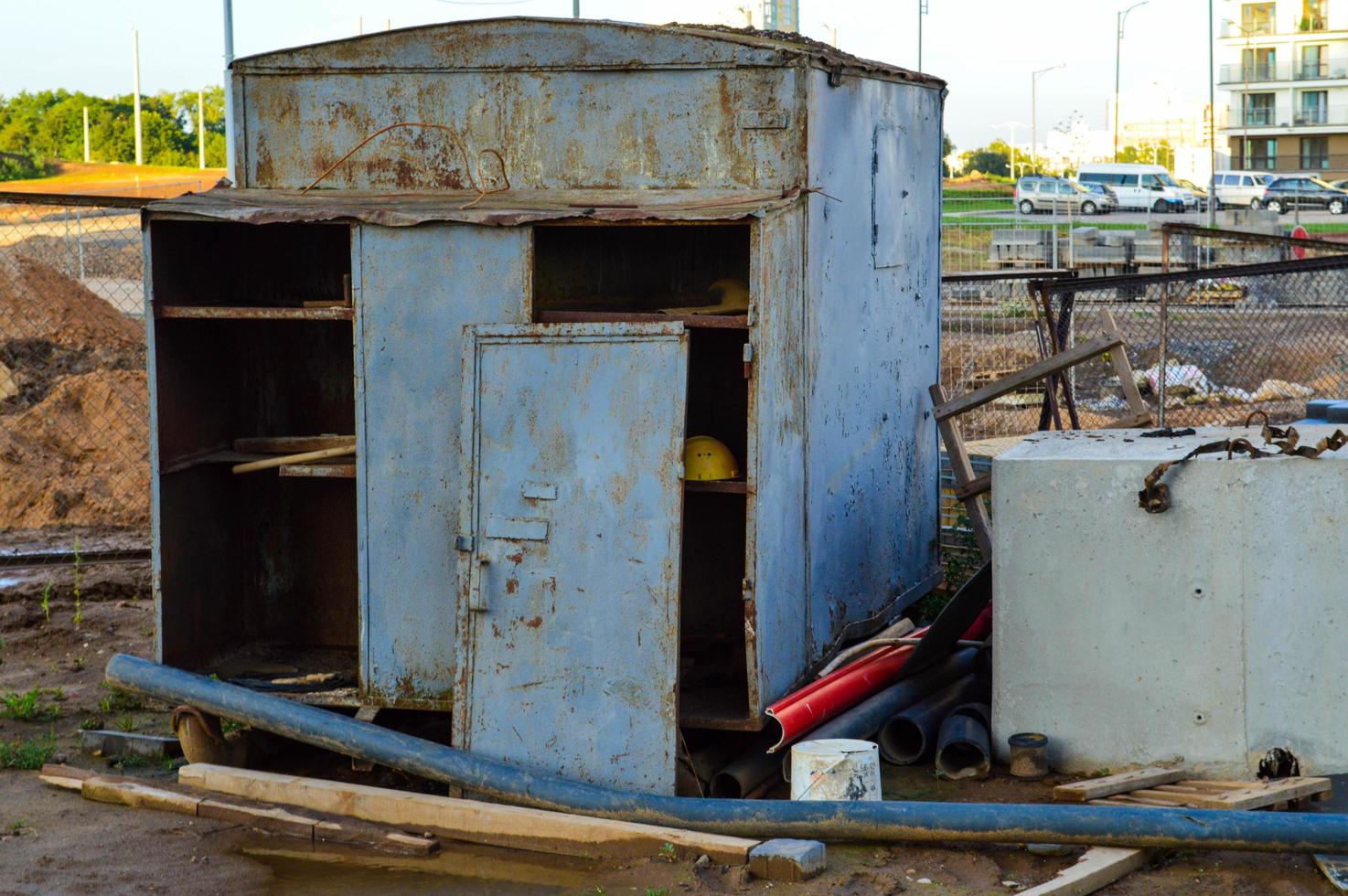 a small metal garage stands in the city at a construction site. a carriage for the life of builders, with a small kitchen and a sleeping place. the trailer is rusted, there are pipes nearby photo