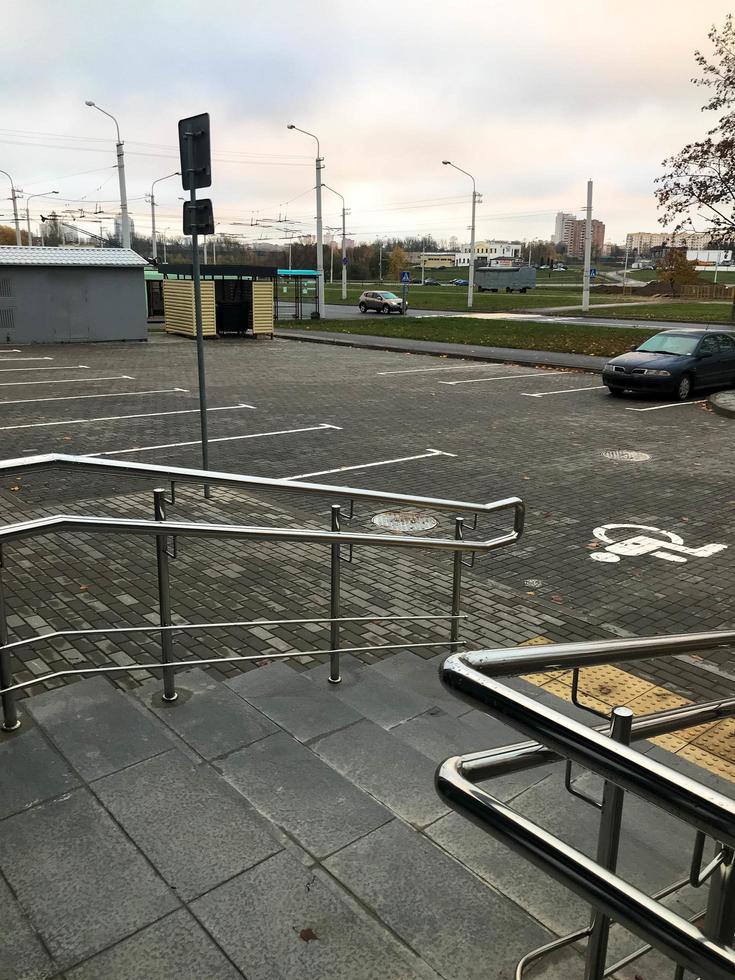 porch, access to the parking lot from the public building. spacious parking lot with a place for disabled people. walk at dawn. black metal railings. parking near the bus stop and trash cans photo