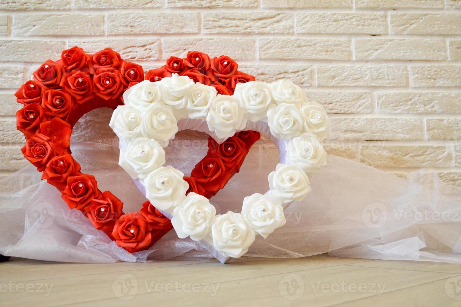 Two hearts. Red and white hearts with a pattern of roses with diamonds on a background of a beige brick wall. photo