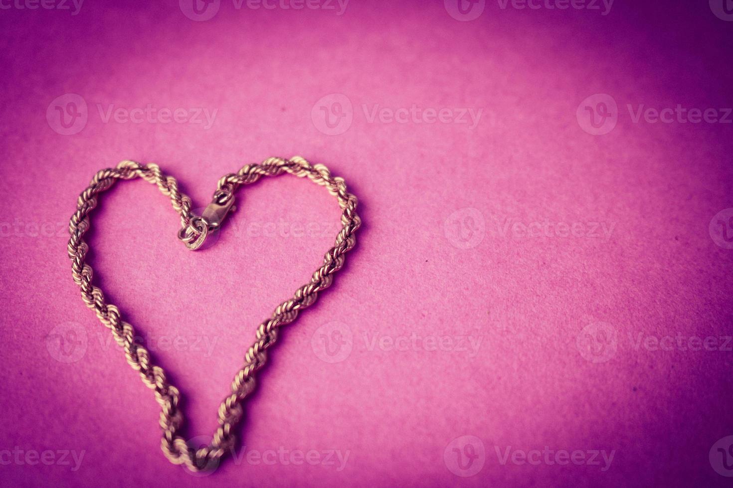 Texture of a beautiful golden festive chain unique weaving in the shape of a heart on a pink purple background and copy space. Concept love, marriage proposal, marriage, St. Valentine's Day photo