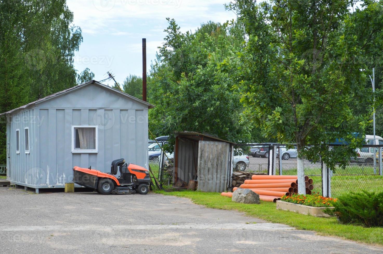 A large professional agricultural lawn mower, a lawn mowing tractor with grass, stands near the tool shed photo