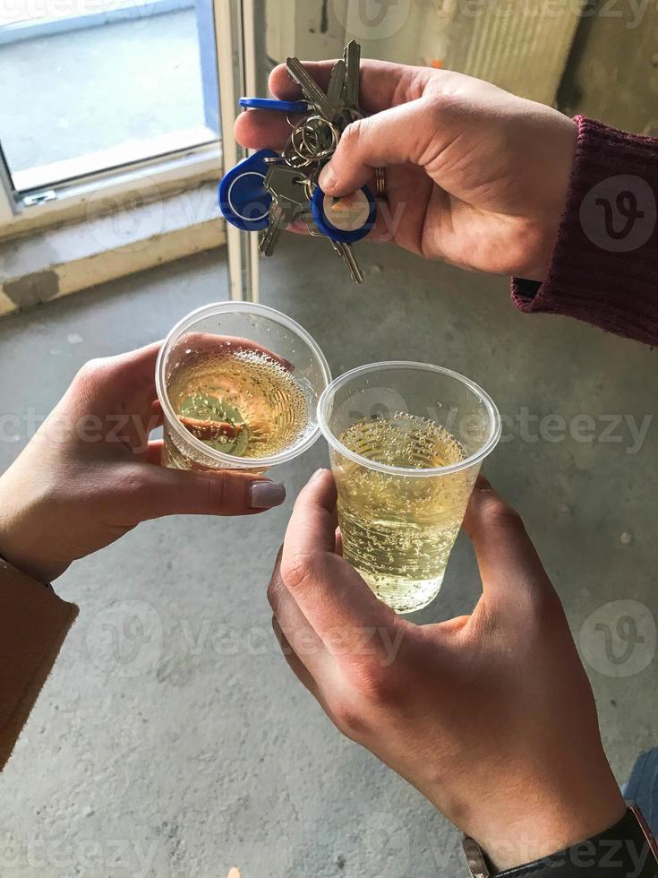 A young family, the hands of a man and a woman hold plastic disposable cups and clink glasses of champagne, celebrate the receipt of the keys to the house, apartment. Housewarming concept photo