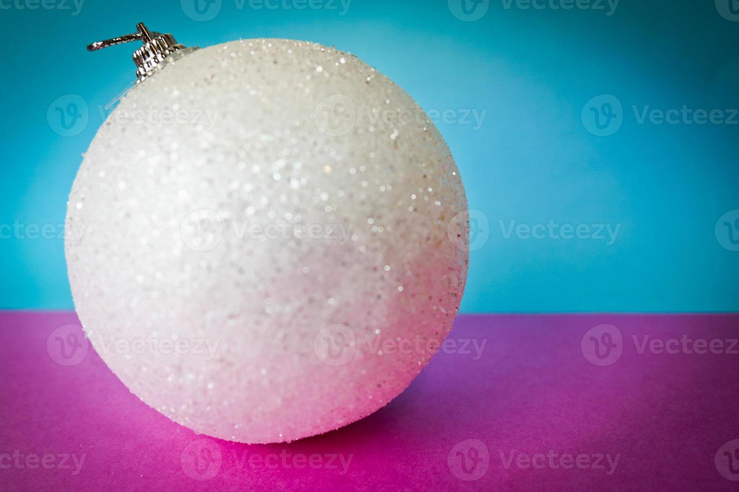 White snow small round glass plastic winter smart shiny decorative beautiful xmas festive Christmas ball, Christmas toy plastered over sparkles on a pink purple blue background photo