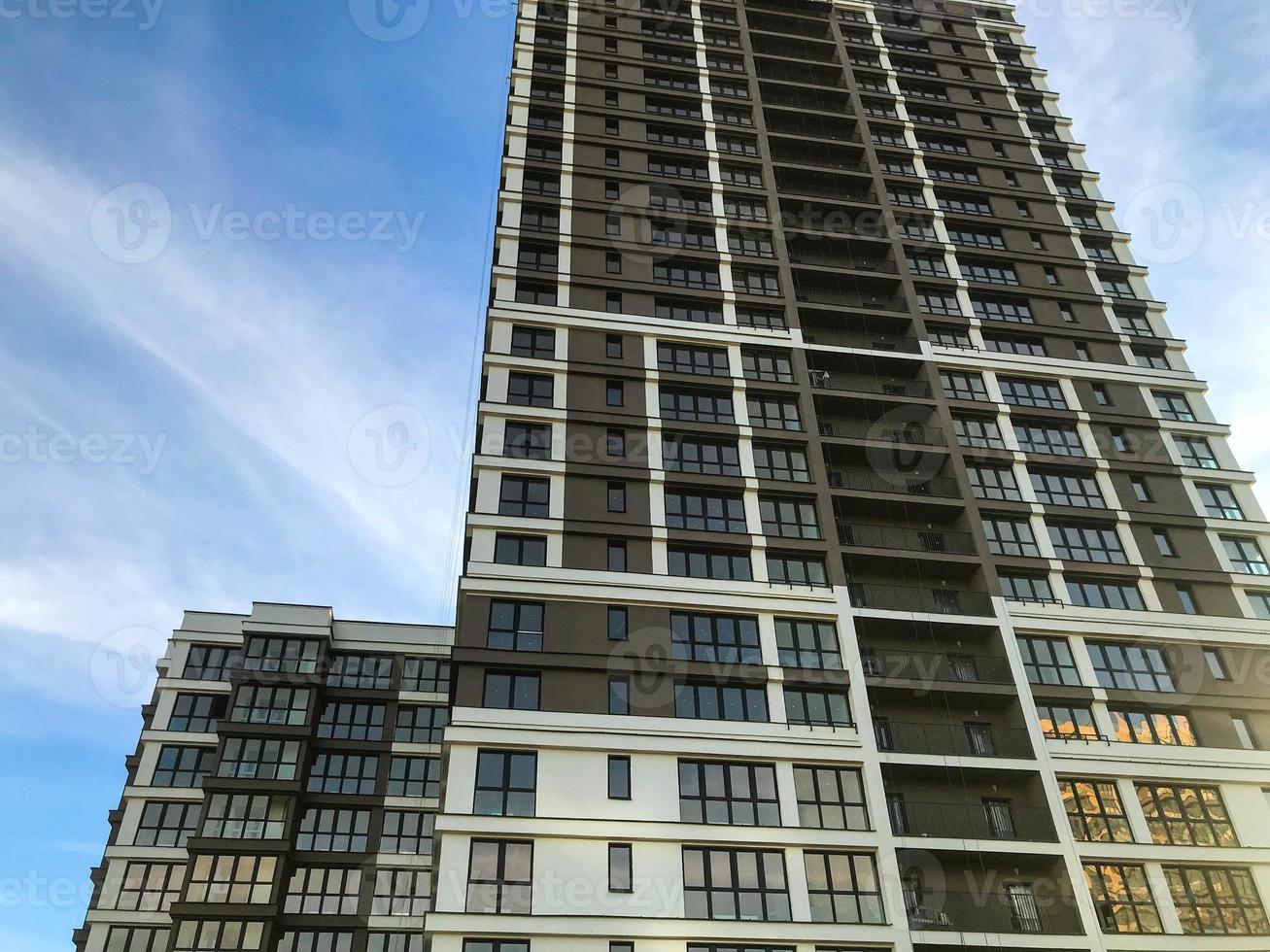 edificio de varios pisos marrón y blanco en el centro de la ciudad. hay un pequeño edificio al lado del edificio de gran altura. transición de casa en casa a lo largo del puente. contra el cielo azul foto