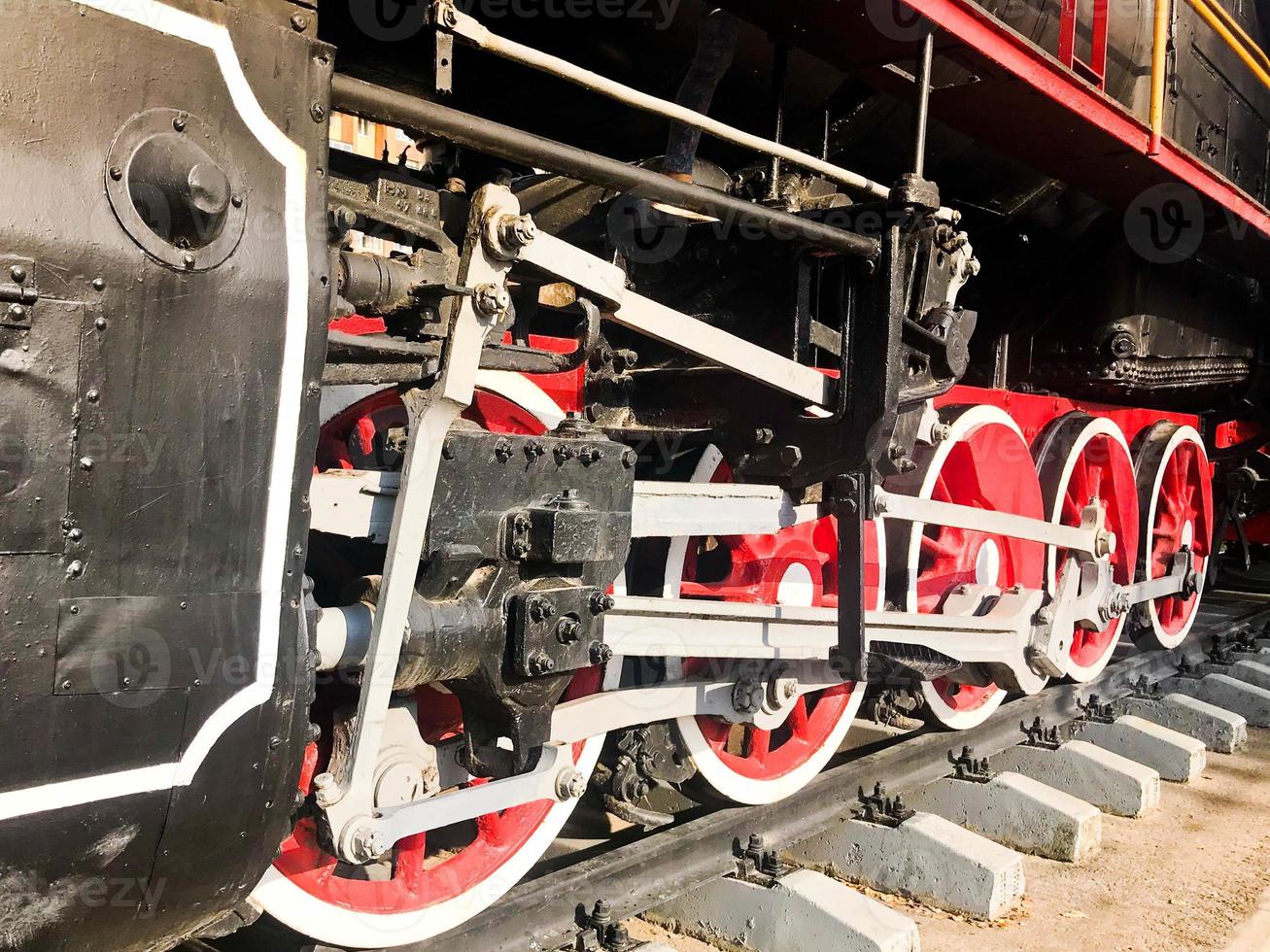 Large iron wheels of a red and black train standing on rails and suspension elements with springs of an old industrial steam locomotive photo