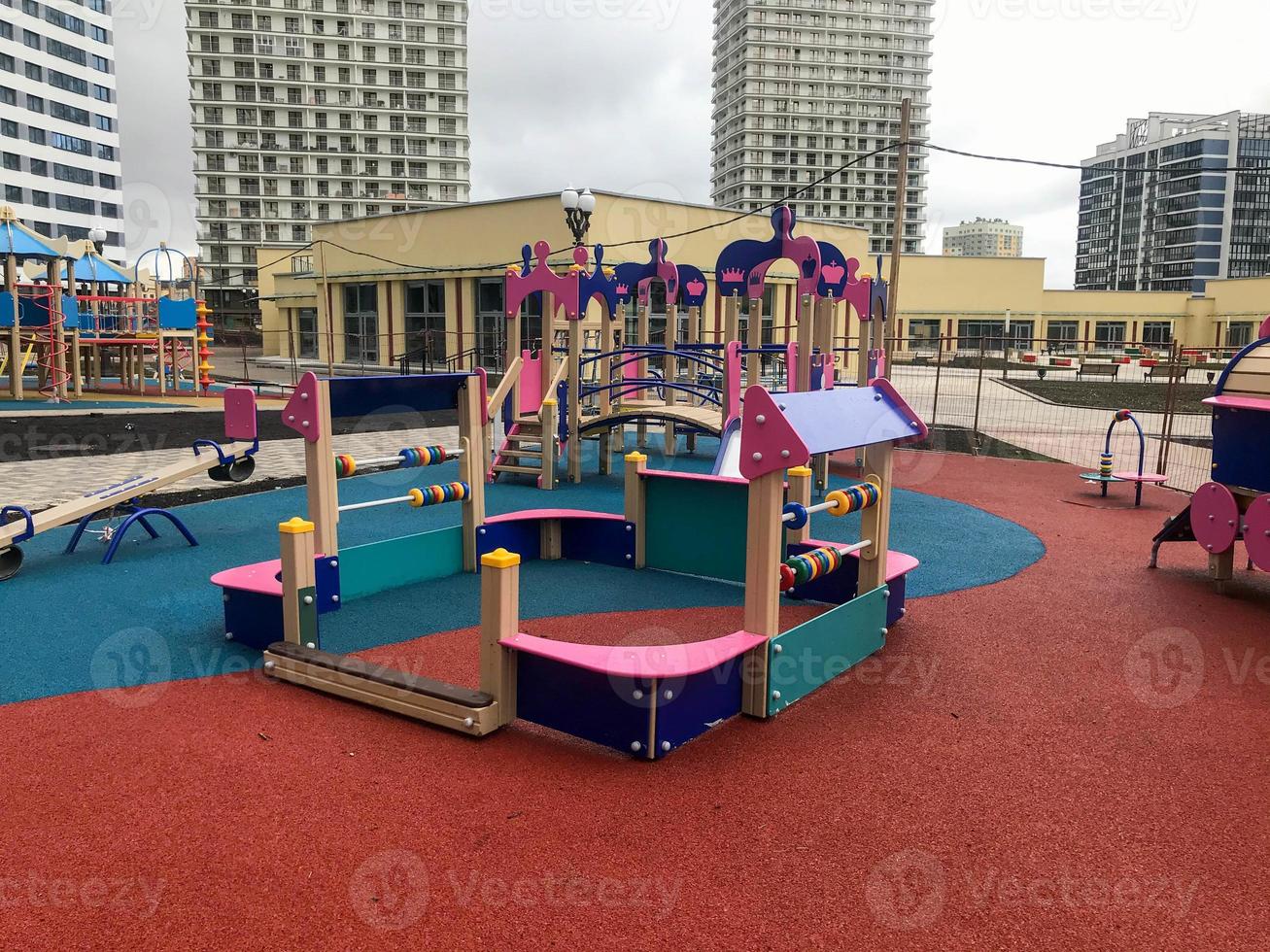children's pink playground in the center of the residential complex. for kids there are swings, abacus, fun slides and climbing frames. playground next to the mall and tall white houses photo