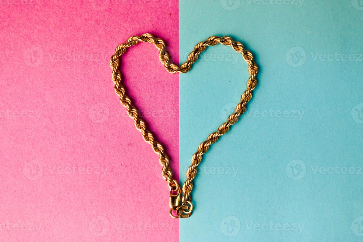 Texture of a beautiful golden festive chain unique weaving in the shape of a heart on a pink purple blue background and copy space. Concept love, marriage proposal, marriage, St. Valentine's Day photo