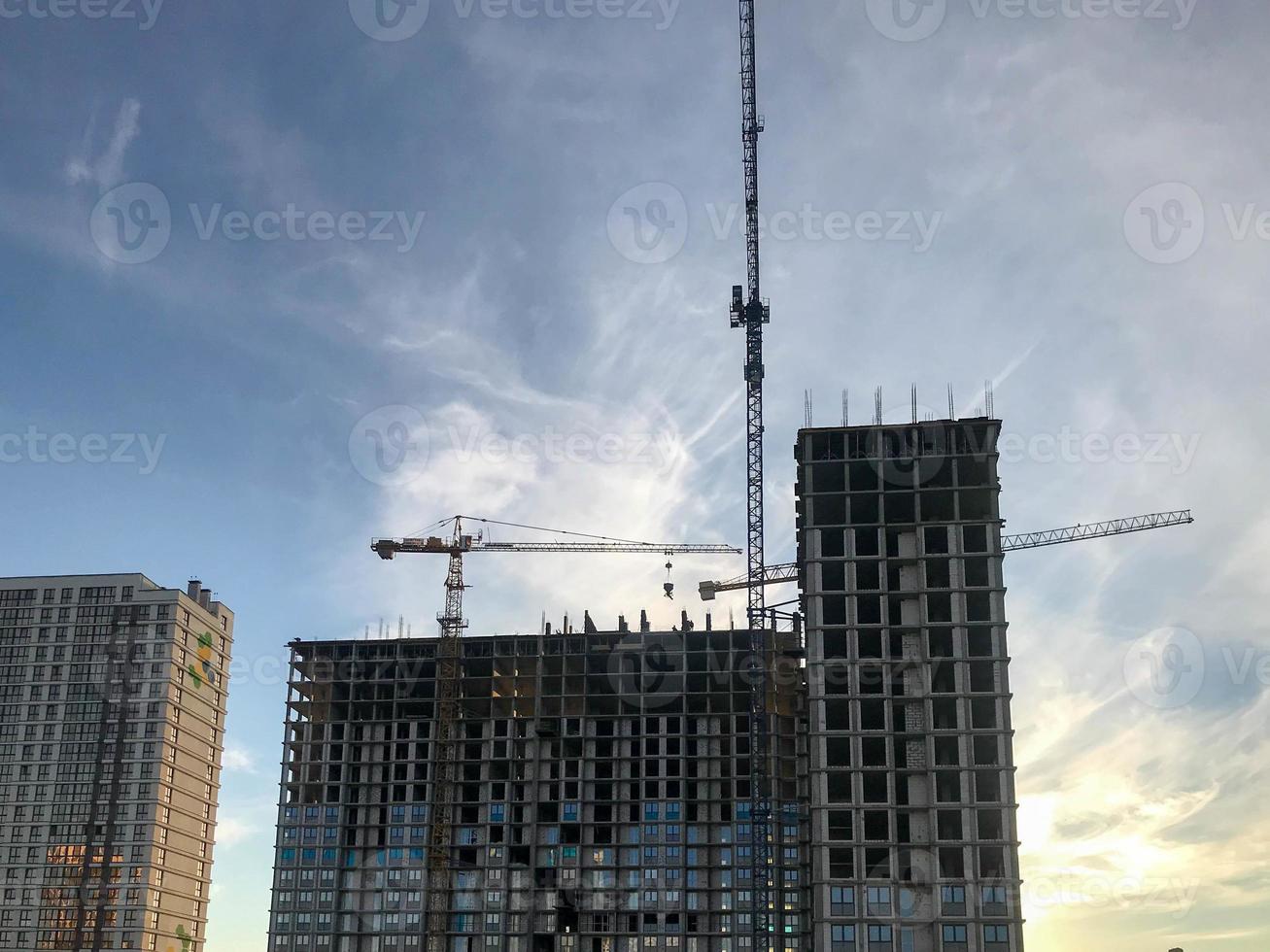 construction cranes are erecting new houses from heavy cellular blocks. construction of a new area. construction landscape. gray houses without painting. against the blue sky photo