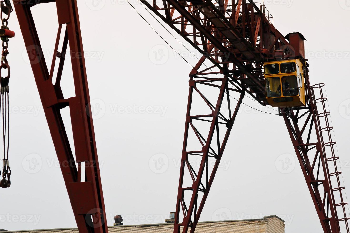 Industrial iron large metal gantry crane with a hook mounted on the supports for lifting and carrying heavy cargo, moving along the rails at the factory. The crane is of bridge type photo