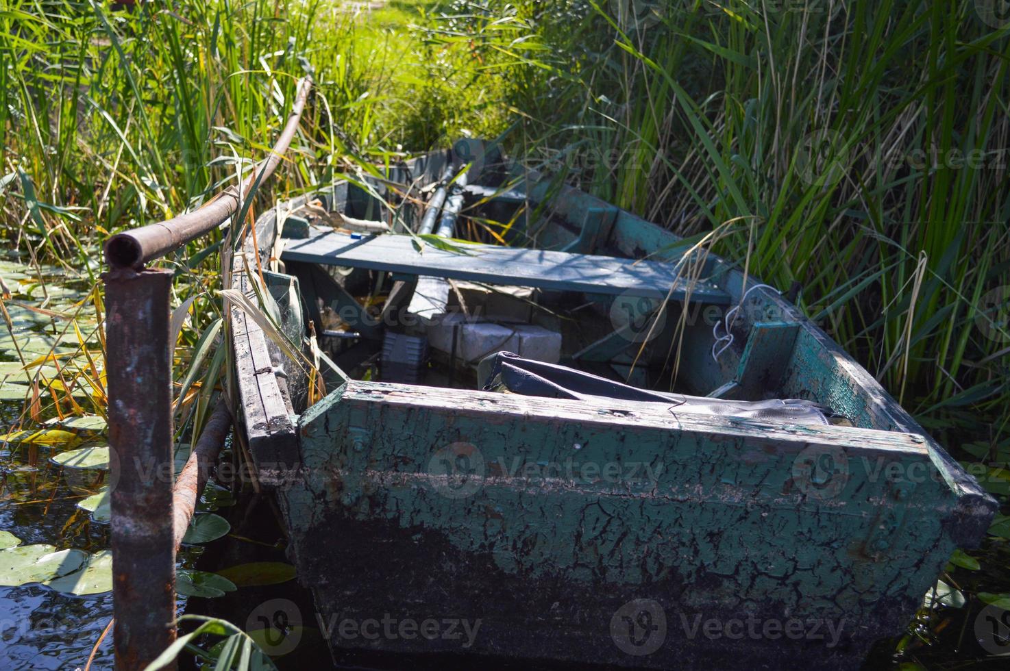 Old wooden shabby dilapidated broken boat for swimming on the banks of the river, lake, sea in the grass and reeds in nature photo