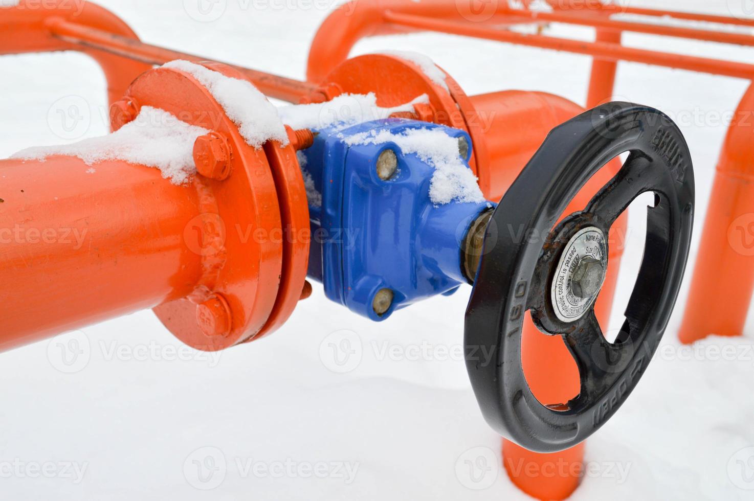 Industrial shut-off regulating protective pipe fittings. Black valve for opening, closing on an iron orange metal pipe with flanges, studs, nuts against the background of white snow in winter photo