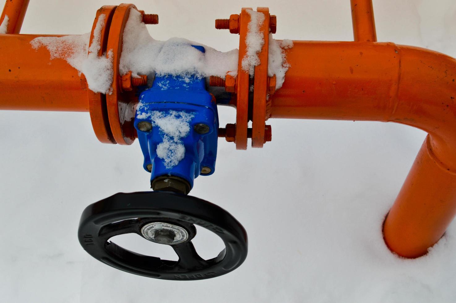 Industrial shut-off regulating protective pipe fittings. Black valve for opening, closing on an iron orange metal pipe with flanges, studs, nuts against the background of white snow in winter photo