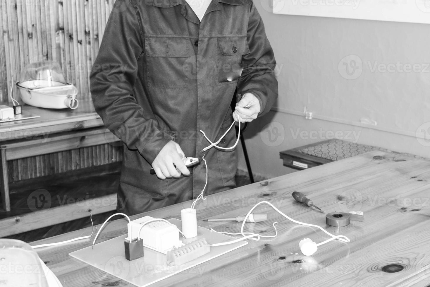 A man working electrician works, collects the electric circuit of a large white street lamp with wires, a relay at an industrial plant factory photo