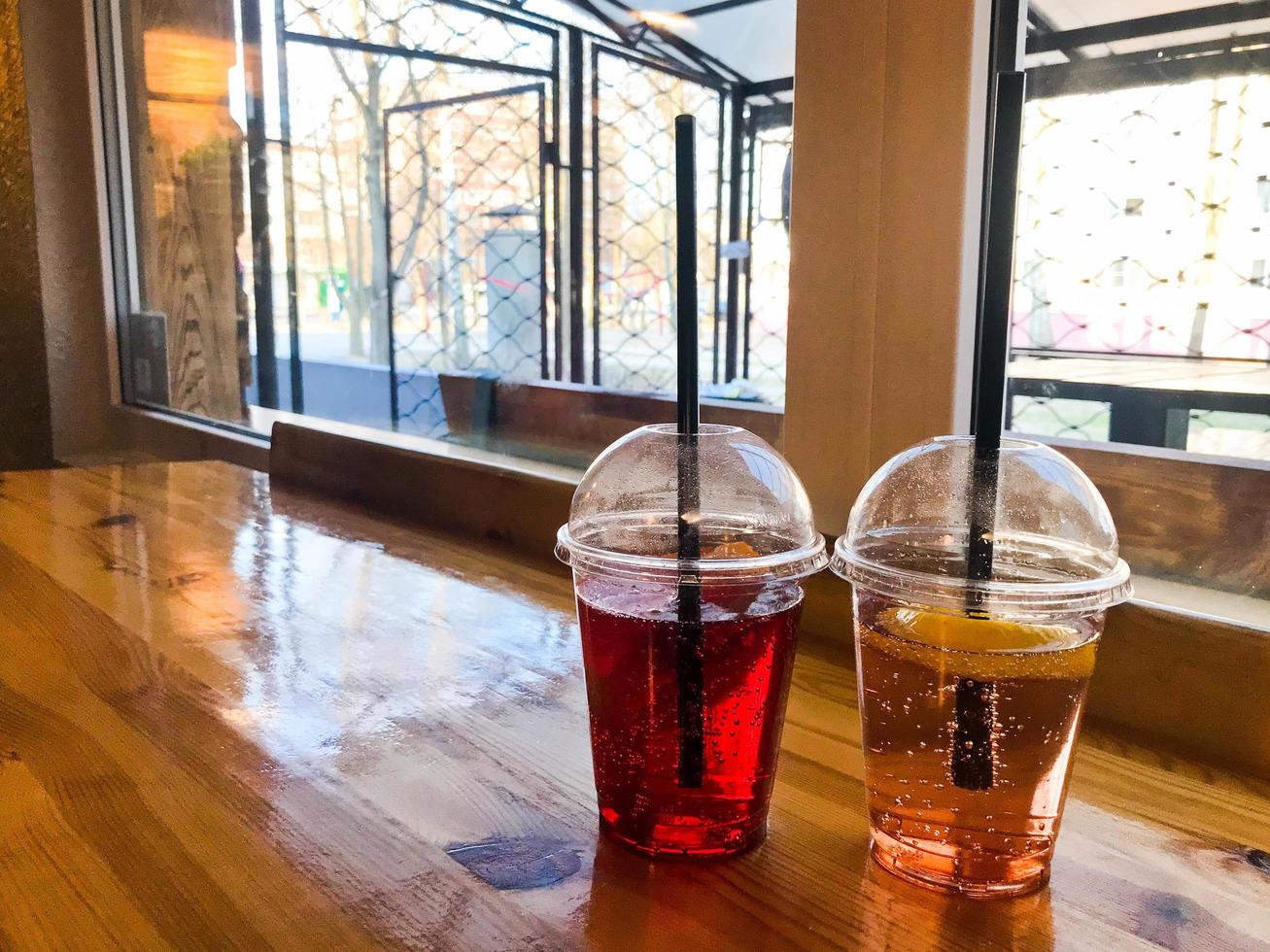 Two glasses of plastic red and yellow refreshing cold tasty sweet raspberry strawberry cherry orange peach lemon fruit lemonade natural with a straw and syrup bubbles photo